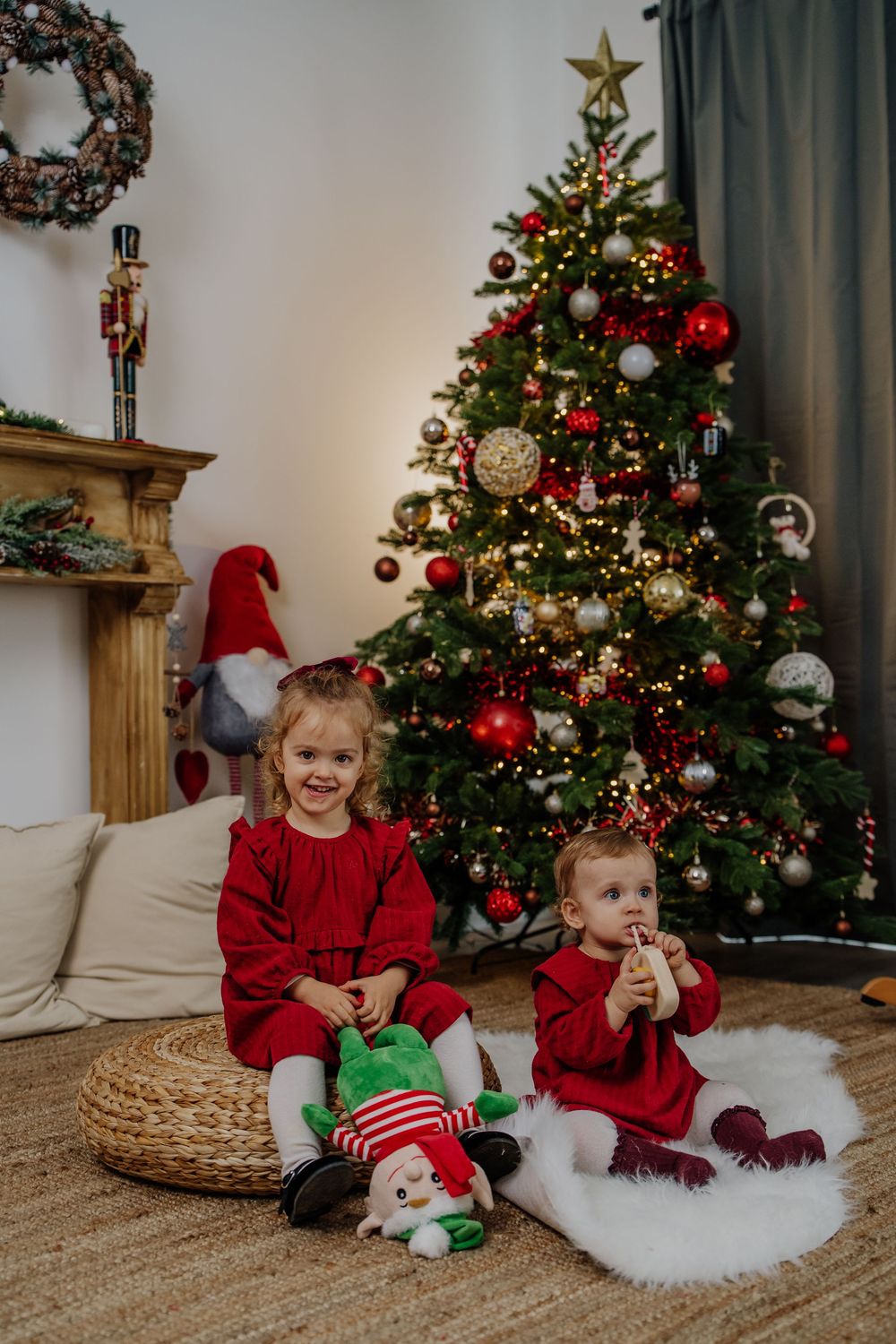 Duas irmãs de vestido vermelho sentadas junto à árvore de Natal