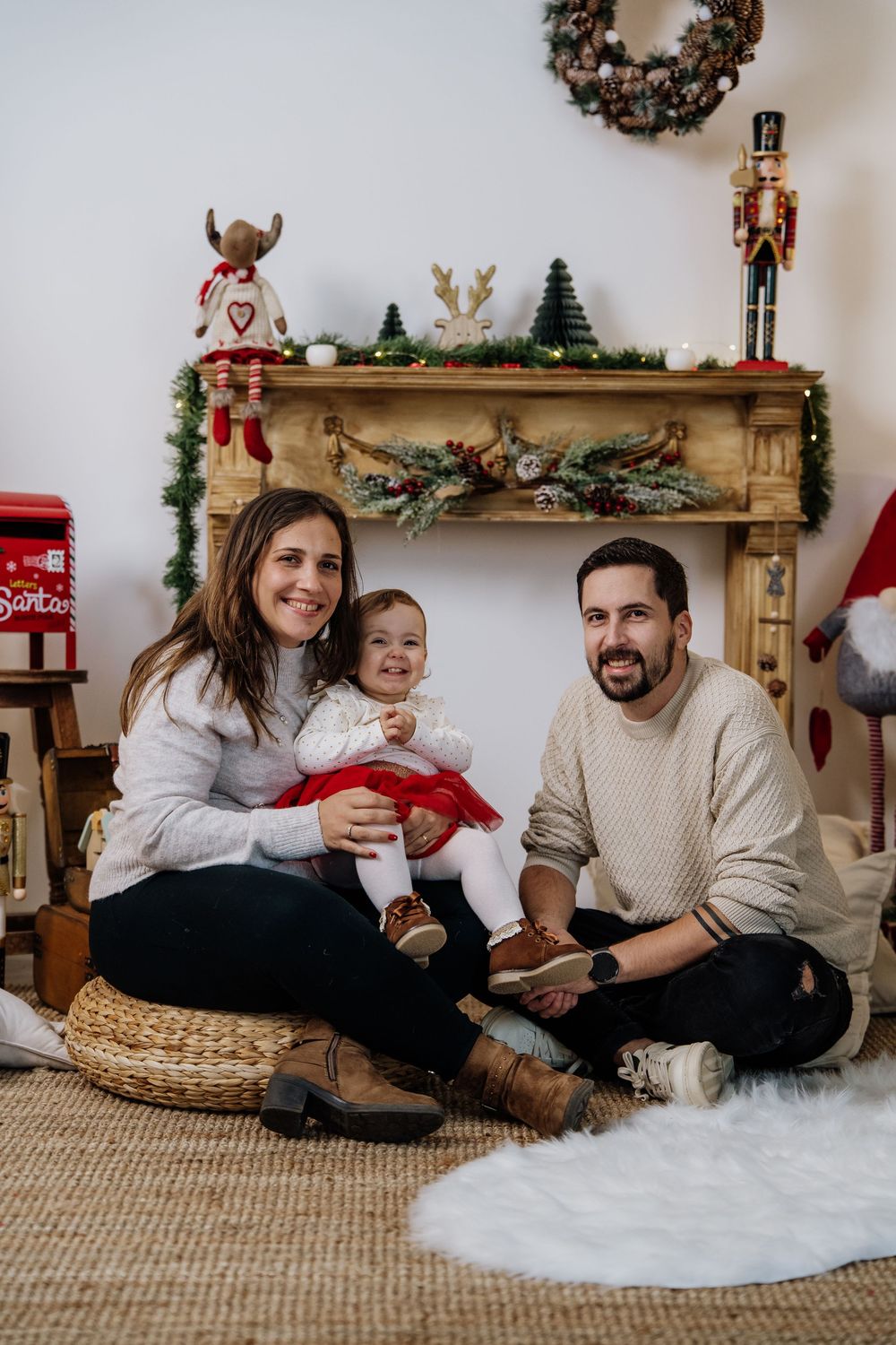 Família de três sentada junto à lareira decorada de Natal