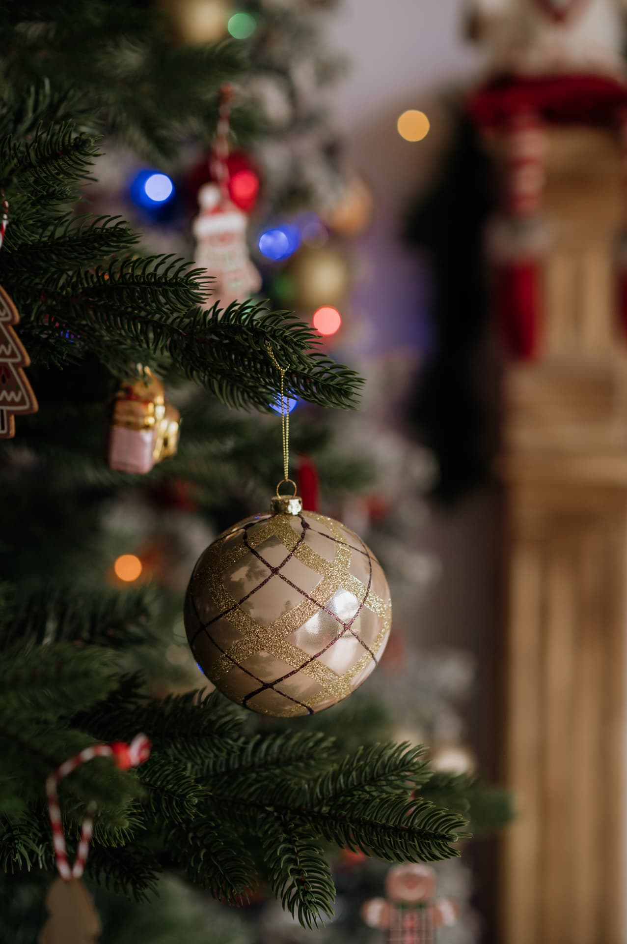 Detalhe de árvore de Natal: bola champanhe com riscas douradas pendurada num ramo de pinheiro, com luzes desfocadas ao fundo